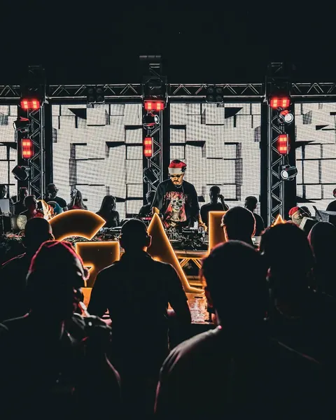 DJ de gorro de Natal na mesa, com painel de LED atrás e o público em silhueta