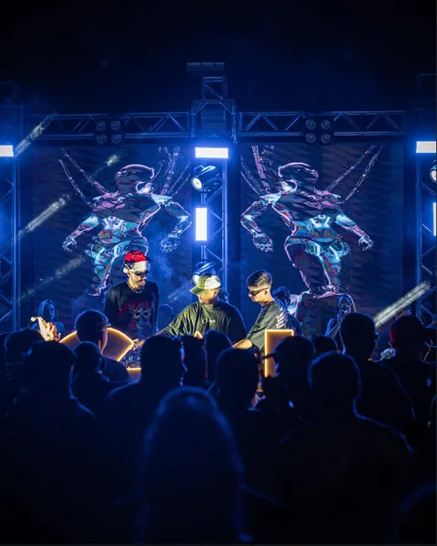 Trio de DJs no palco com painel de LED, treliça de luz azul e o público